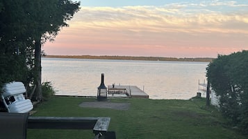 Relax on the lakeside deck with a bench and table, surrounded by lush greenery and a serene view of the water.