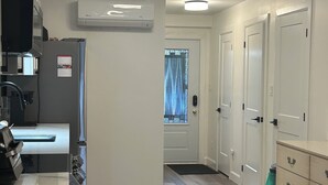 Eine moderne Küche mit Einbauofen, Mikrowelle und Kühlschrank. Ein Fenster mit Vorhang, eine Tür mit Fußmatte sowie ein Flur zu mehreren Schränken.