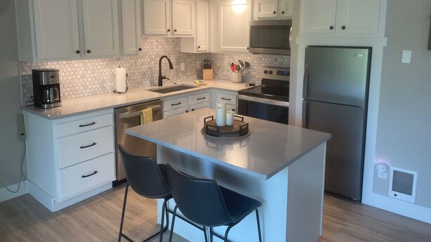 Una cocina moderna con armarios blancos, un refrigerador de acero inoxidable, una cafetera y una zona de bar con dos sillas.