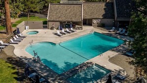 Un área de piscina con dos piscinas, sillones de descanso y un edificio con techo inclinado.