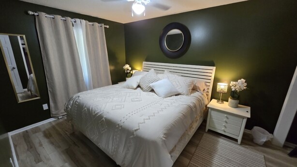 Une chambre à coucher avec un lit, une table de chevet, un miroir et un ventilateur de plafond.
