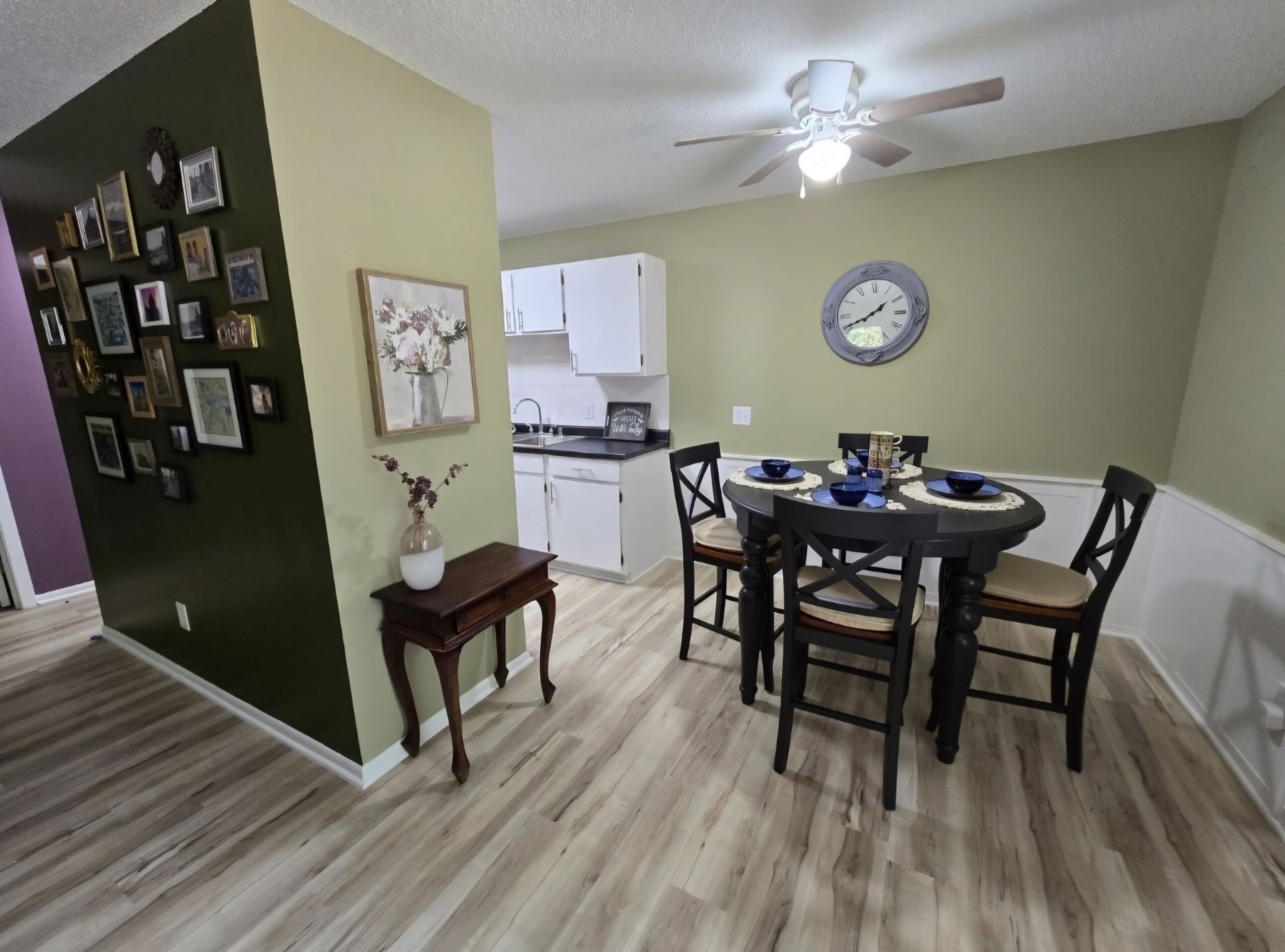 Un coin repas comprenant une table ronde, des chaises, un ventilateur de plafond et une horloge murale.