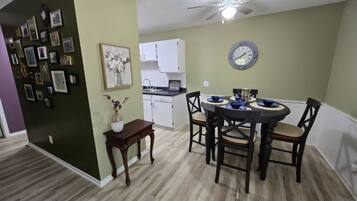 Un coin repas comprenant une table ronde, des chaises, un ventilateur de plafond et une horloge murale.