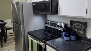 Une cuisine de taille réduite avec des meubles blancs, un réfrigérateur en acier inoxydable, un four à micro-ondes et une cuisinière. On peut voir deux récipients bleus sur le comptoir.