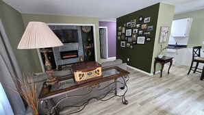 Un salon avec une cheminée, une table basse et un mur décoré de photos.