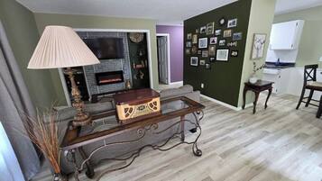 Un salon avec une cheminée, une table basse et un mur décoré de photos.
