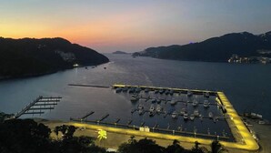 A marina with boats docked, surrounded by hills and a sunset in the background.