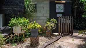 A small outdoor seating area with potted plants, a chalkboard with opening hours, and a sign for 'Sublime Farm & Brewery'. - Tiny Sublime by Tiny Away (Kia Ora)