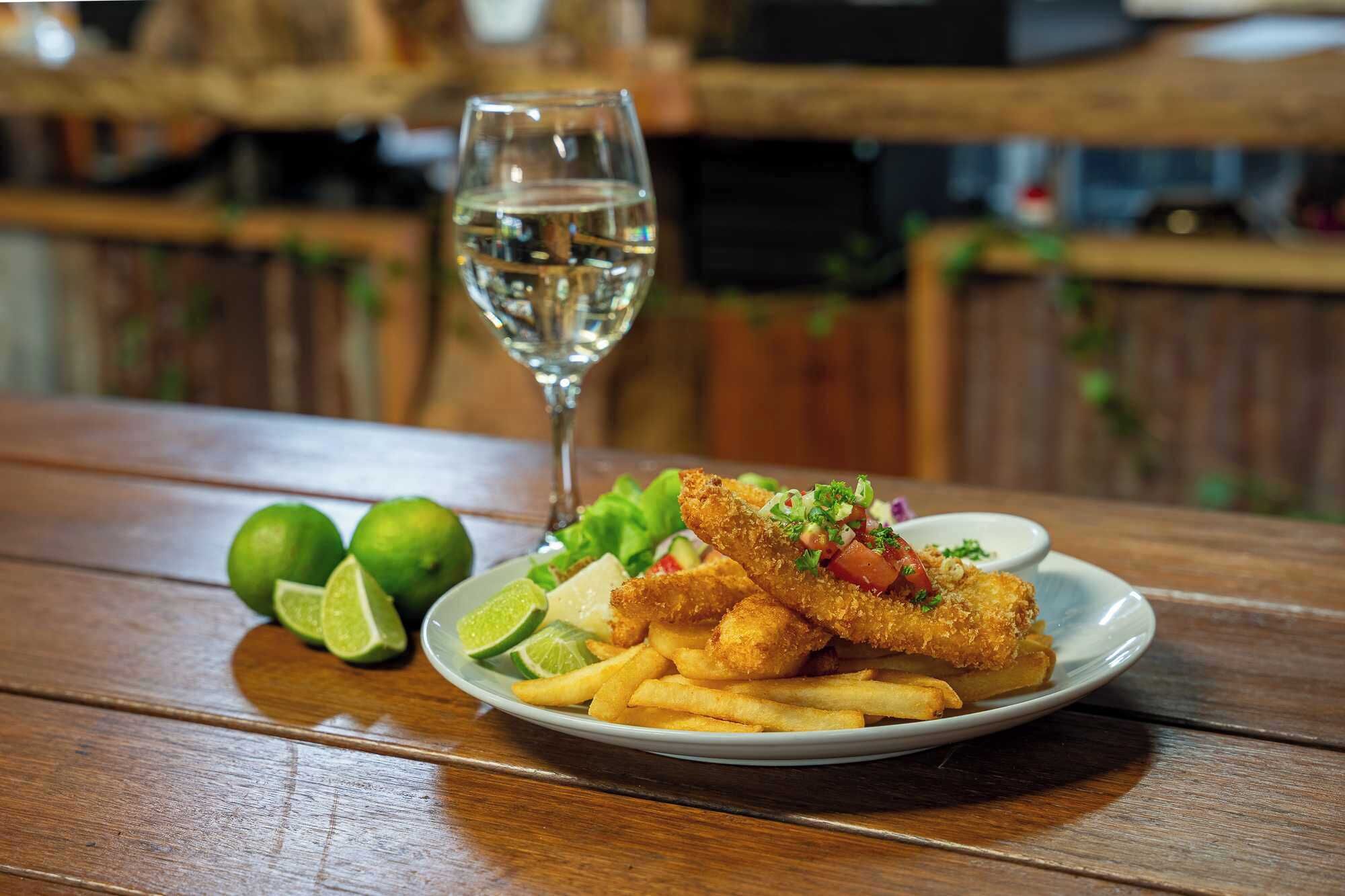 Une assiette de poisson frit, de frites et un verre d’eau sur une table en bois, avec des citrons verts.