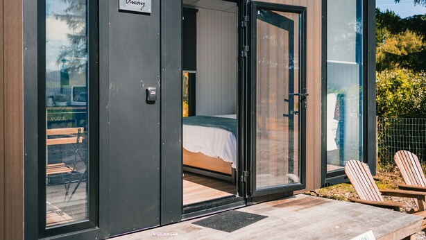 A modern room with a bed, a bench, and a table outside.