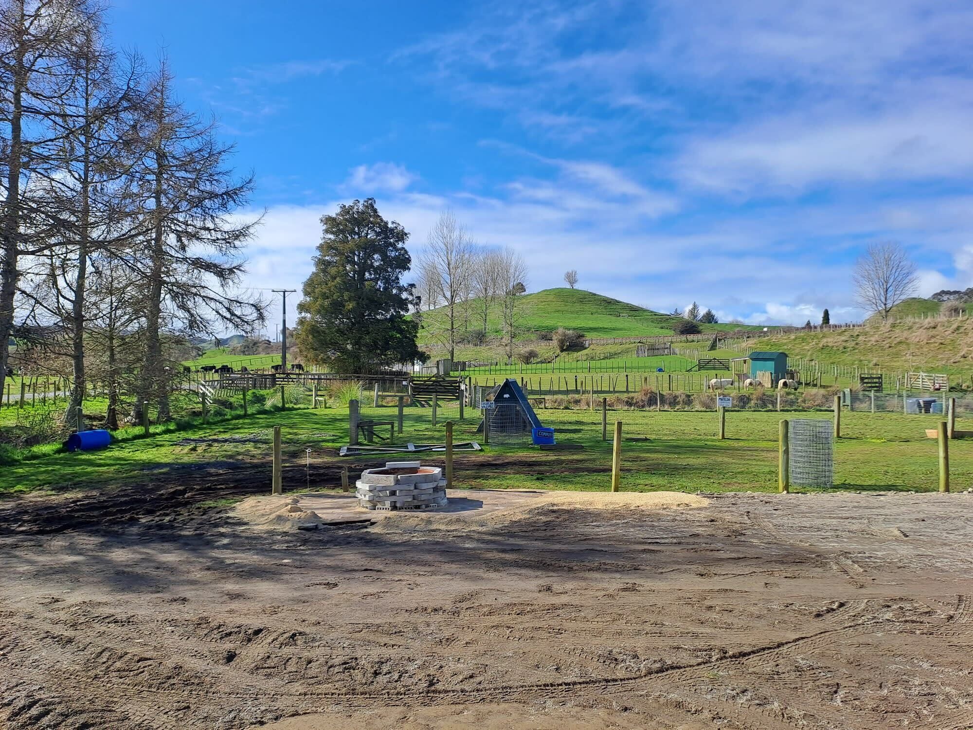 A rural landscape with a fenced area, a small building, and a hill in the background.