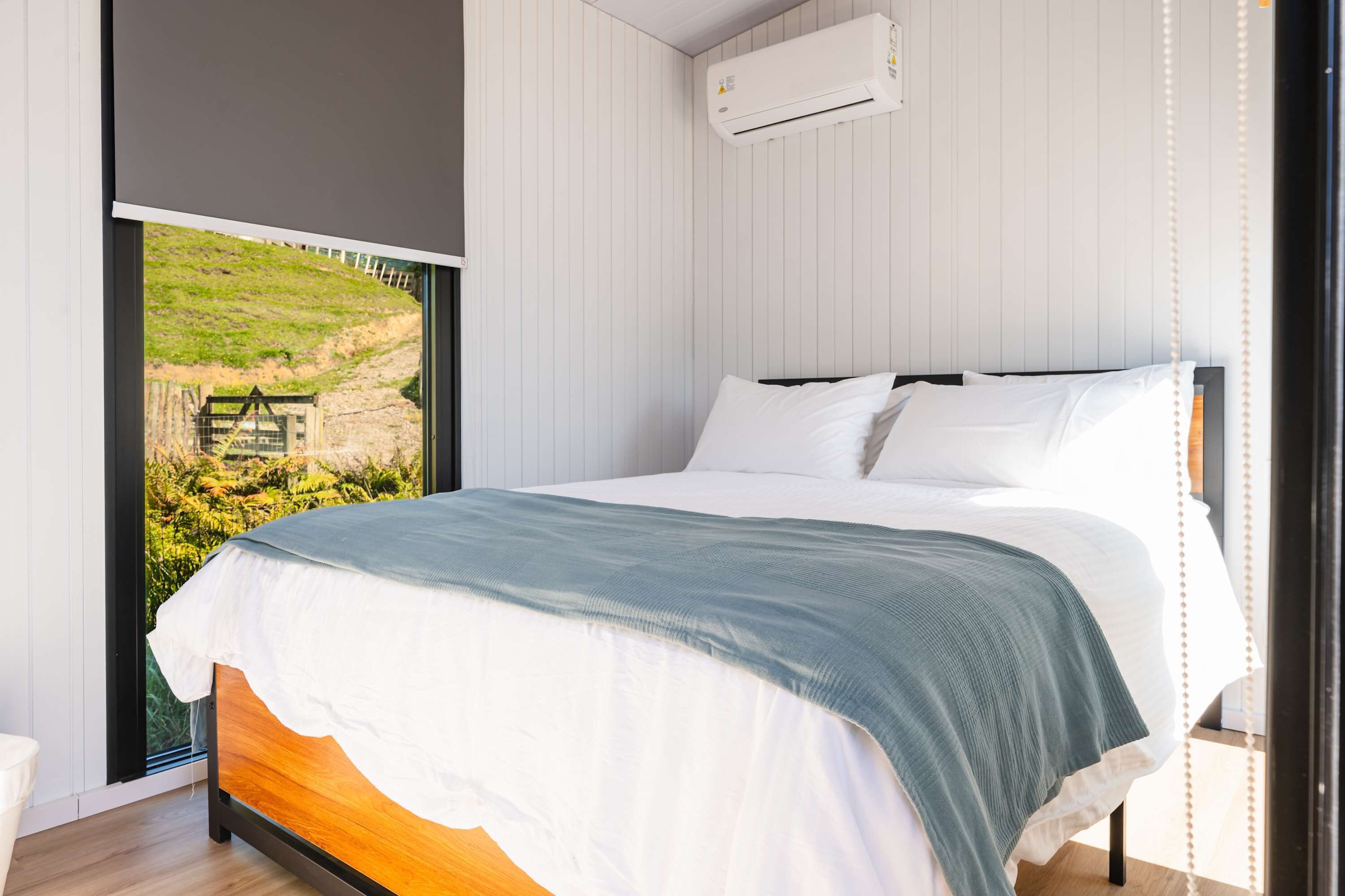Quarto com uma janela grande, cama com roupa de cama branca e ar condicionado na parede.