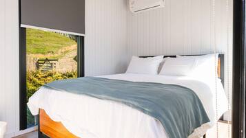 Quarto com uma janela grande, cama com roupa de cama branca e ar condicionado na parede.