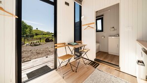 A modern room with a wooden floor, a small table with chairs, a view of a vineyard, and a kitchen area with a sink and cabinets.