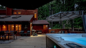 Une terrasse en bois avec un jacuzzi, des sièges d’extérieur et un bâtiment doté de fenêtres.