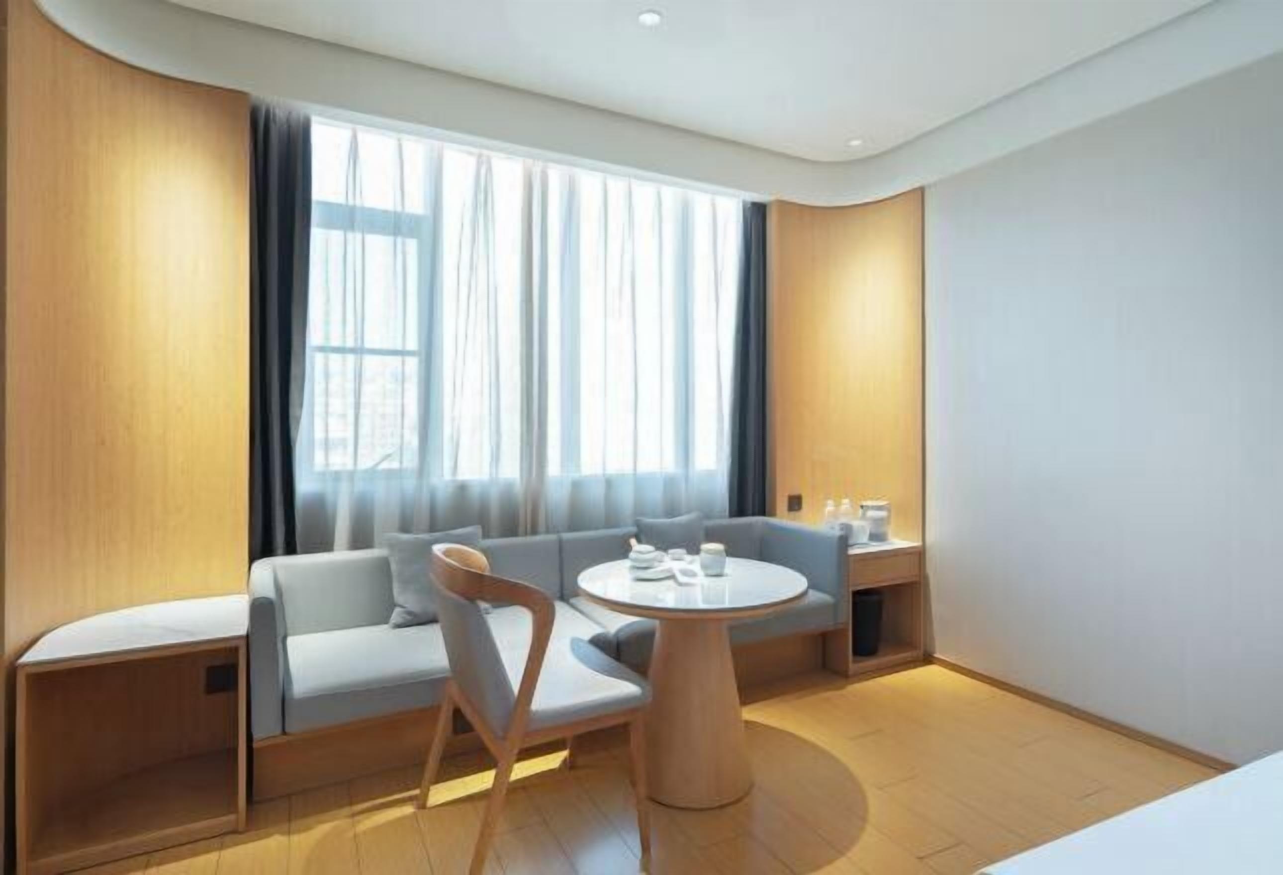 A modern hotel room with a sofa, a round table, and a window with curtains.
