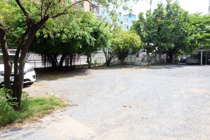 A paved parking area with trees and a fence in the background. - OYO 75429 '101 Place Navanakorm' (Khlong Luang)