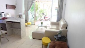 A modern living room with a sofa, a small table, and a yellow stool. There is a desk with a chair and a potted plant. - OYO 75429 '101 Place Navanakorm' (Khlong Luang)