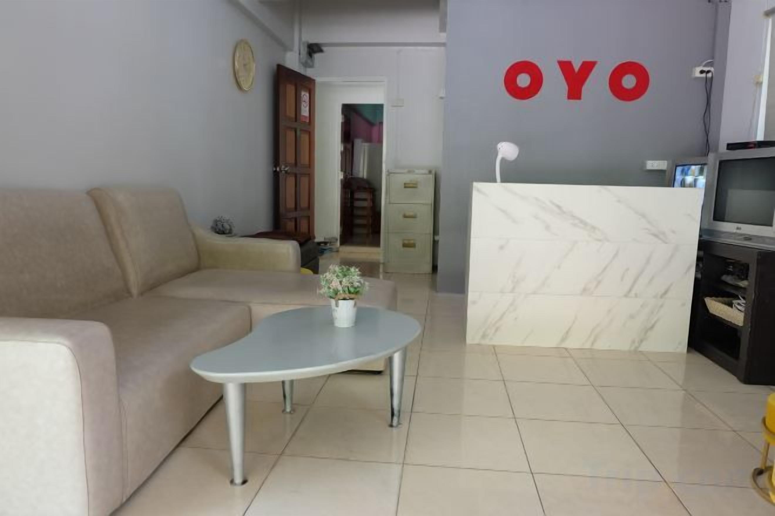Ein Wohnzimmer mit einer Couch, einem Couchtisch mit einer Blume, einer Küchenzeile mit einer Marmorarbeitsplatte und einer Wand mit dem Schriftzug 'OYO'.