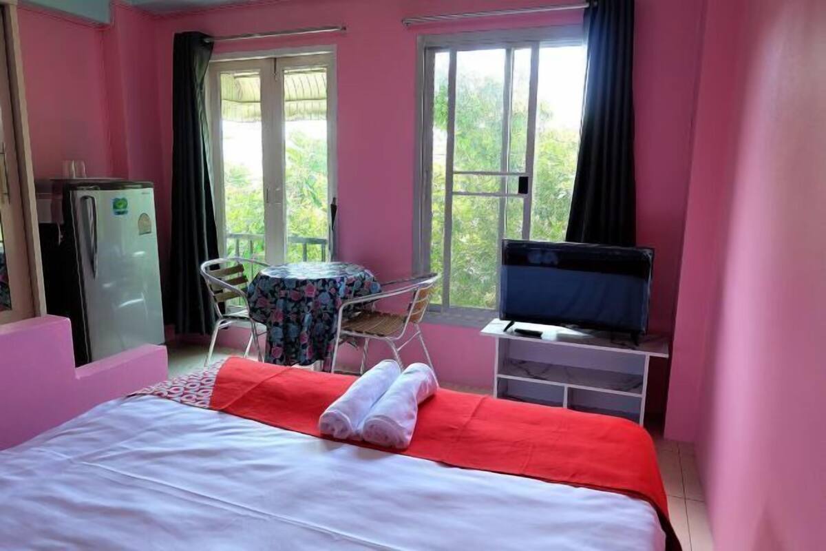 Een slaapkamer met een bed, een televisie, een tafeltje en een koelkast.