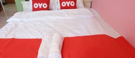 A neatly made bed with red and white bedding, two pillows with 'OYO' text, and a red blanket.