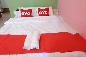 Un lit bien fait, avec une literie rouge et blanche, deux oreillers ornés du mot « OYO » et une couverture rouge.