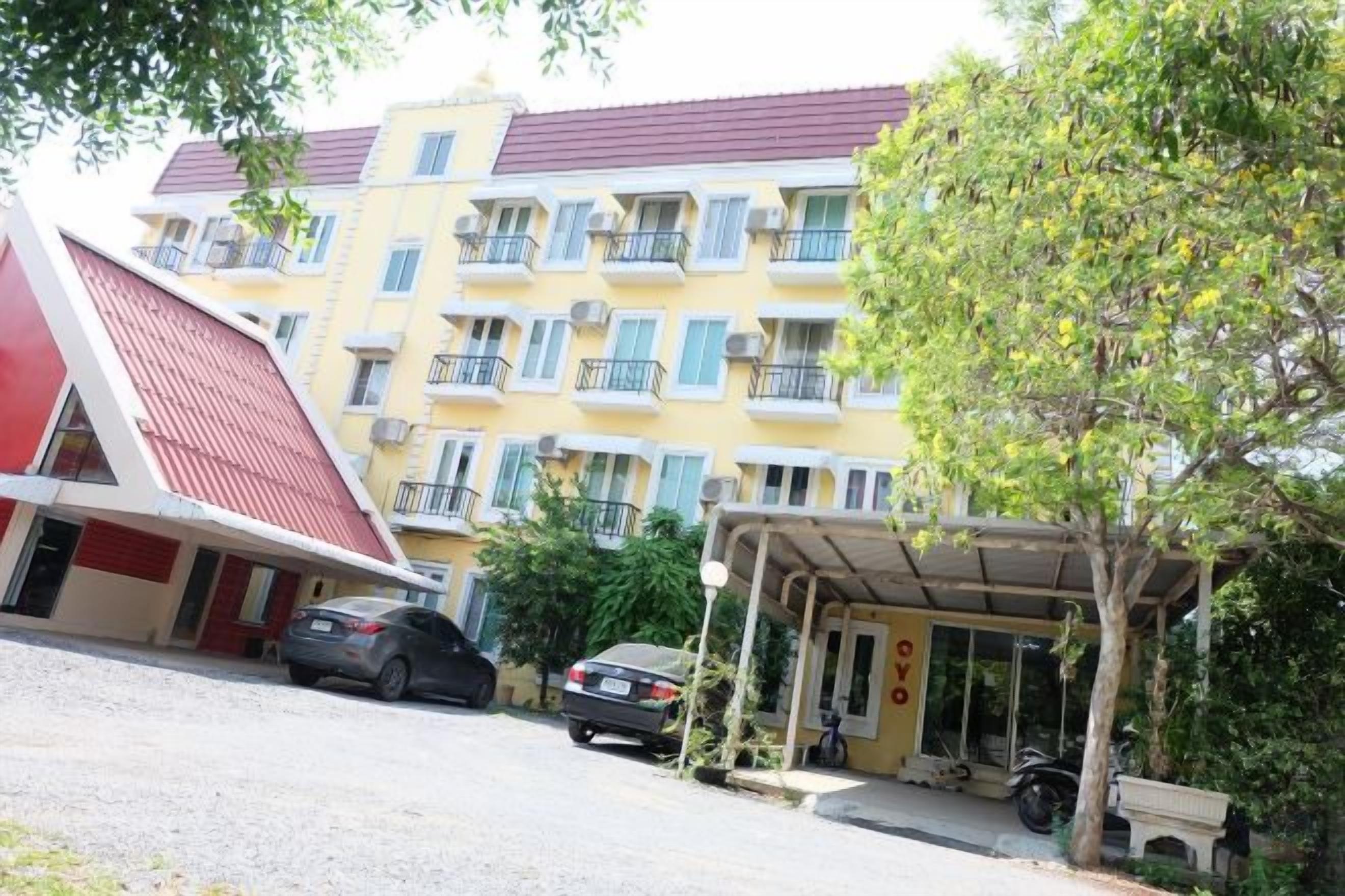 A multi-story hotel with balconies, a covered parking area, and a red-roofed structure.