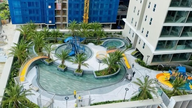 A rooftop pool area with palm trees, a children's play area, and modern buildings in the background. - OYO 75429 '101 Place Navanakorm' (Khlong Luang)