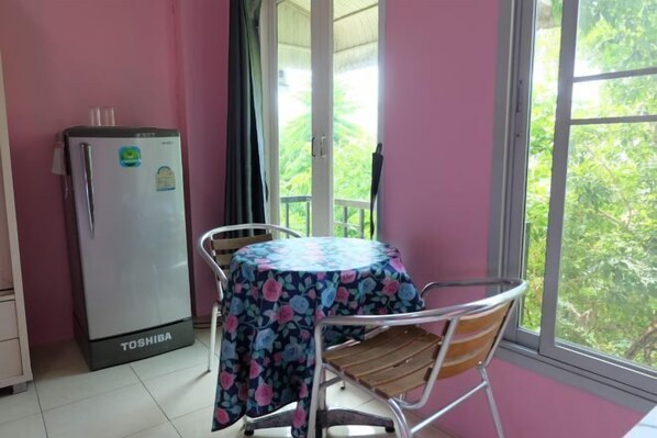 Une pièce dotée d’un réfrigérateur, d’une table recouverte d’une nappe à motifs floraux et d’une fenêtre donnant sur un paysage verdoyant.