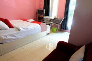 Une pièce comprenant un lit, un téléviseur posé sur un meuble, une chaise, une petite table et une fenêtre avec des rideaux.