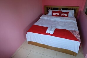 Un lit recouvert d’une couverture rouge et blanche, deux oreillers ornés du mot « OYO » et une serviette enroulée posée sur le lit.