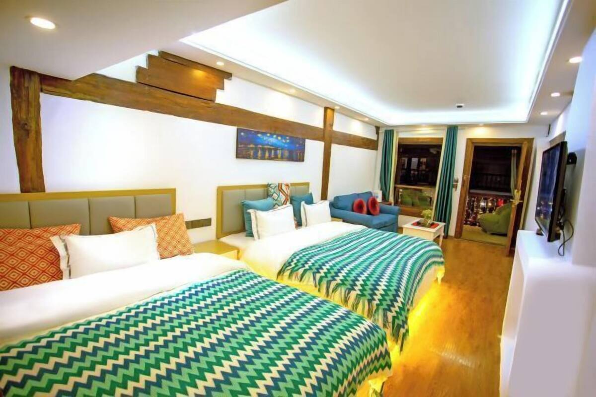 A hotel room with two beds, a sofa, a TV, and a staircase leading to an upper level.