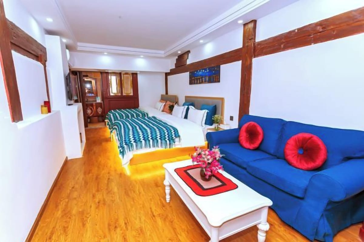 A hotel room with a bed, a blue sofa, a white coffee table, and a wooden floor.