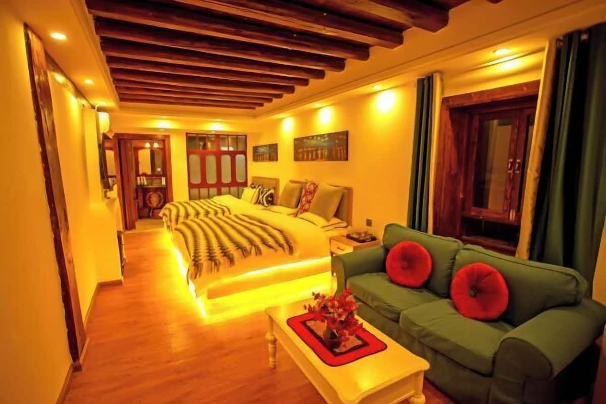 A bedroom with a bed, a green sofa, a wooden floor, and a wooden ceiling.