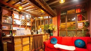 A cozy room with a wooden bar area, a red sofa with blue cushions, and a window with a view of greenery outside. - Good Journey Inn (Shangri-La Guangdong Club) (Shangri-La)
