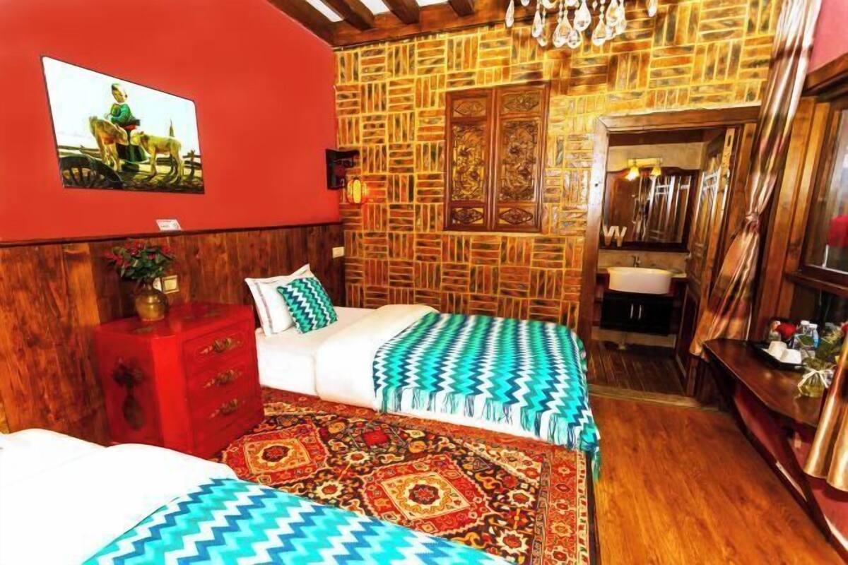 A room with a bed, a red nightstand, a wooden wall with a patterned design, and a mirror.