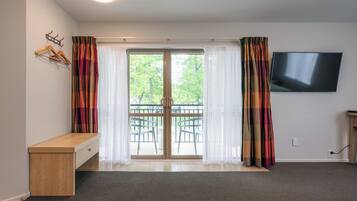 A room with a wooden bench, a TV mounted on the wall, and a sliding glass door leading to an outdoor area with chairs.