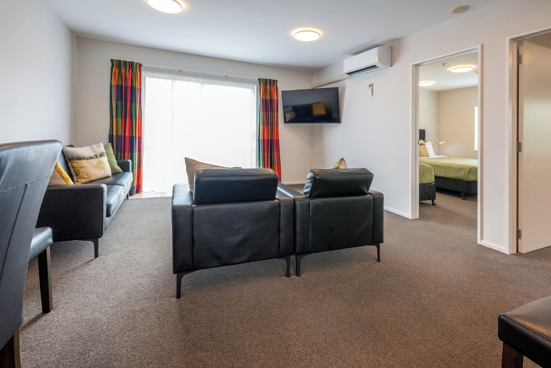 A modern hotel room with a sofa, a chair, a flat-screen TV, and a bed.