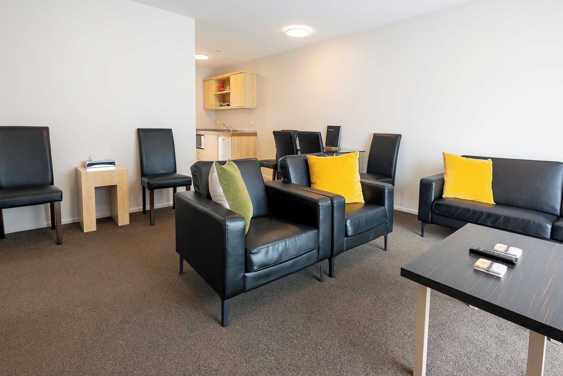 Une chambre d’hôtel moderne, avec un canapé en cuir noir, une table d’appoint en bois, un petit meuble en bois et une table basse noire.