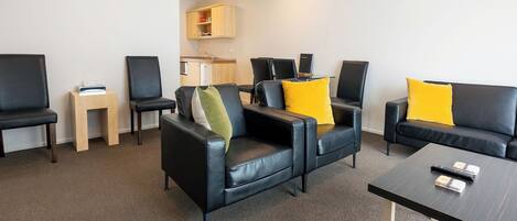 Une chambre d’hôtel moderne, avec un canapé en cuir noir, une table d’appoint en bois, un petit meuble en bois et une table basse noire.