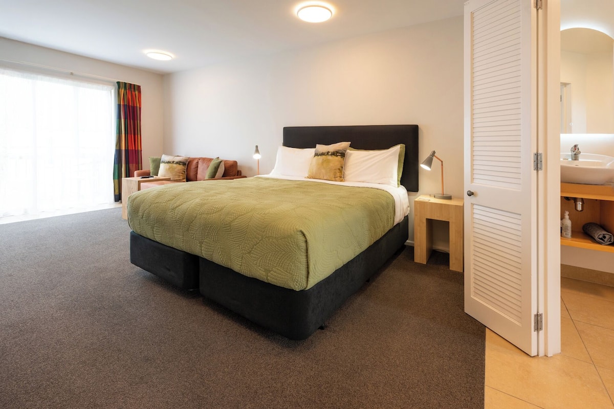 Un dormitorio moderno con una cama grande, una mesita de noche, un tocador y un baño con lavabo y espejo.