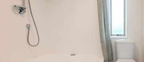 A bathroom with a freestanding bathtub, a showerhead, a toilet, and a window.