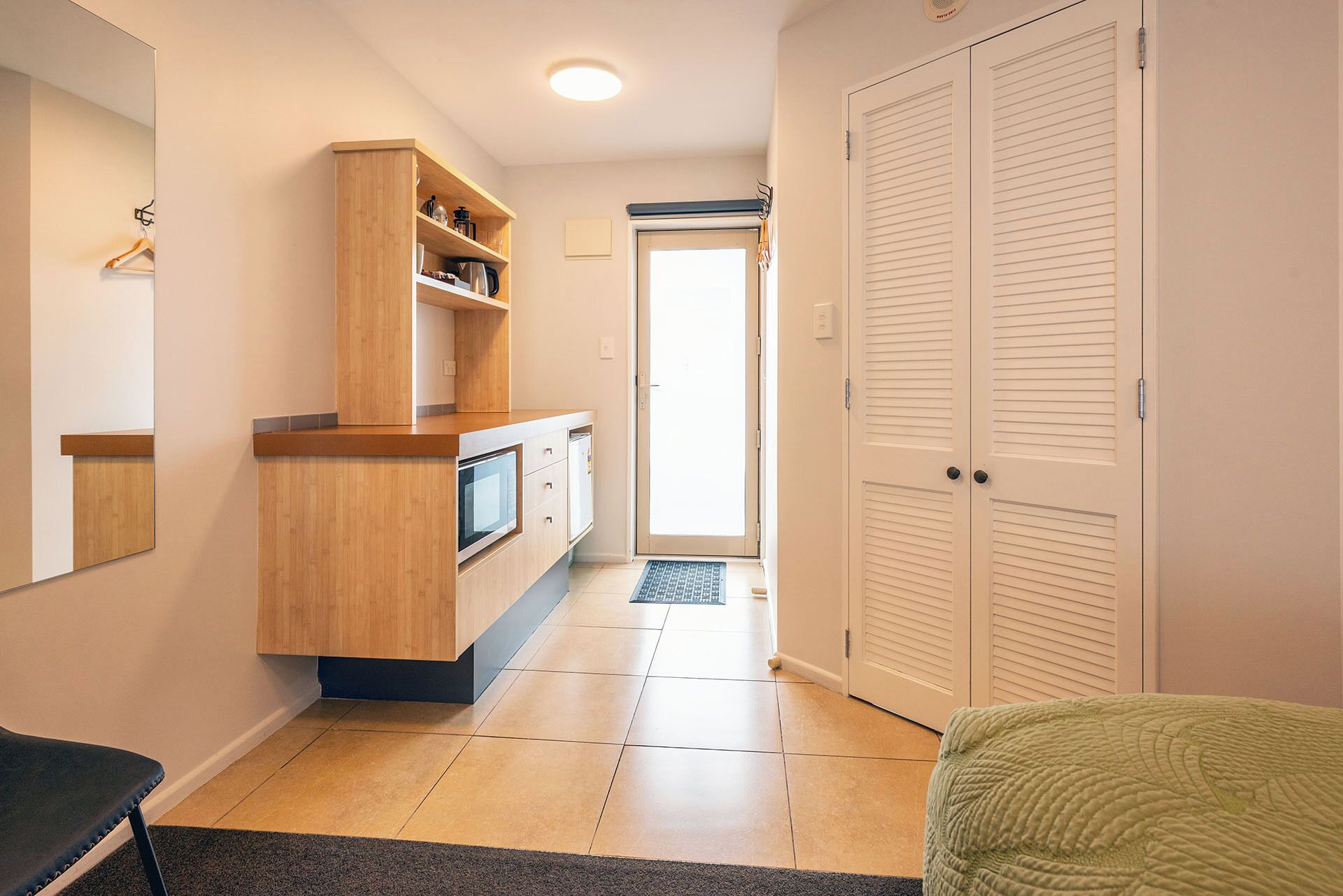 A hallway with a wooden cabinet, a microwave, and a door leading to a room.