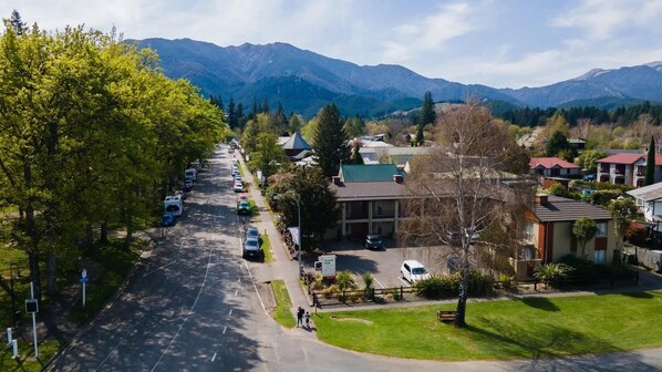 A street view of a town with a hotel in the center, surrounded by residential buildings and mountains in the background. - Tussock Peak Lodge (Hanmer Springs)