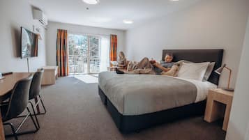Et moderne hotelværelse med en stor seng, et skrivebord og en stol. Der er et vindue med gardiner, et fladskærms-tv monteret på væggen og en loftlampe.