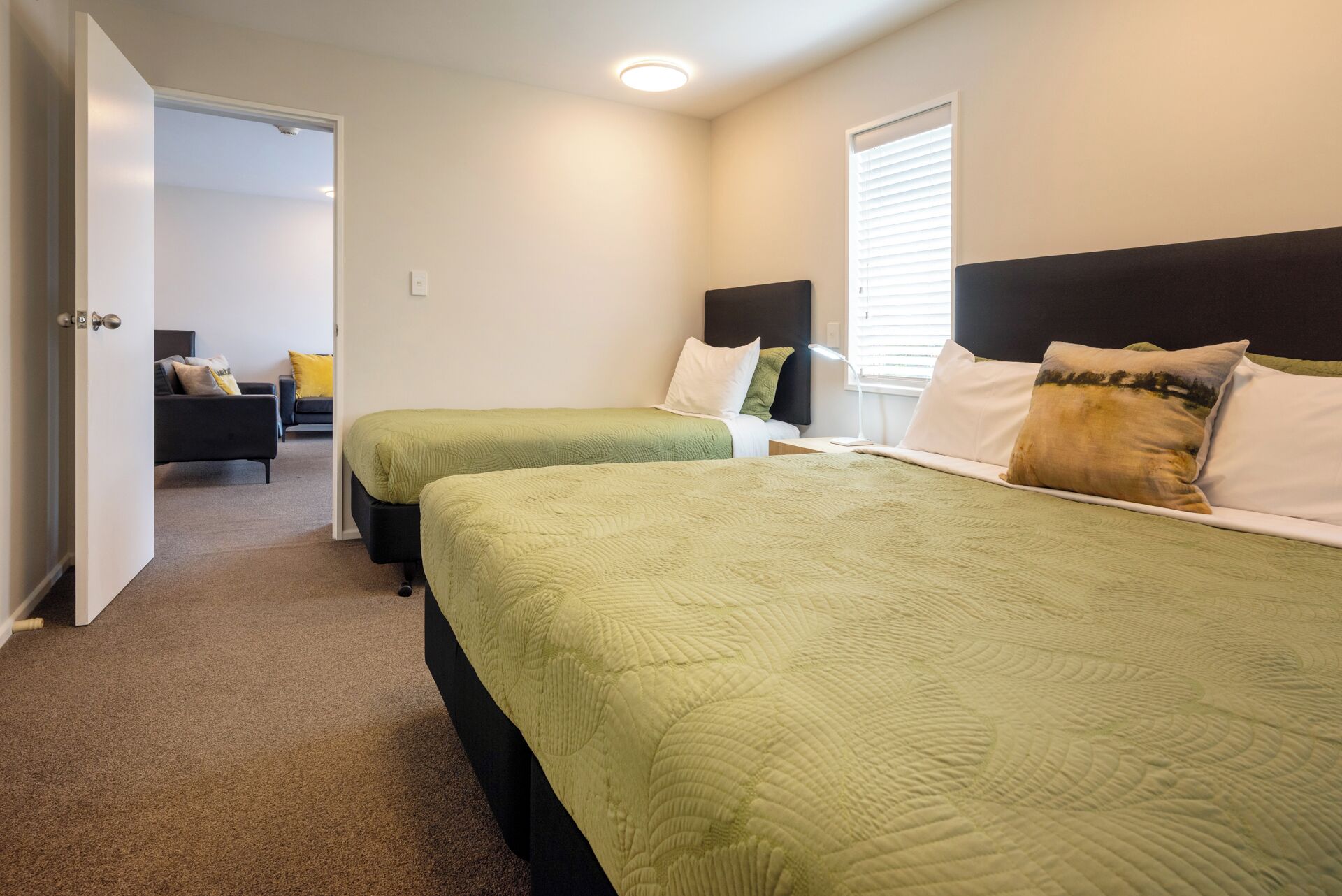 A hotel room with two beds, a sofa, and a window with blinds.