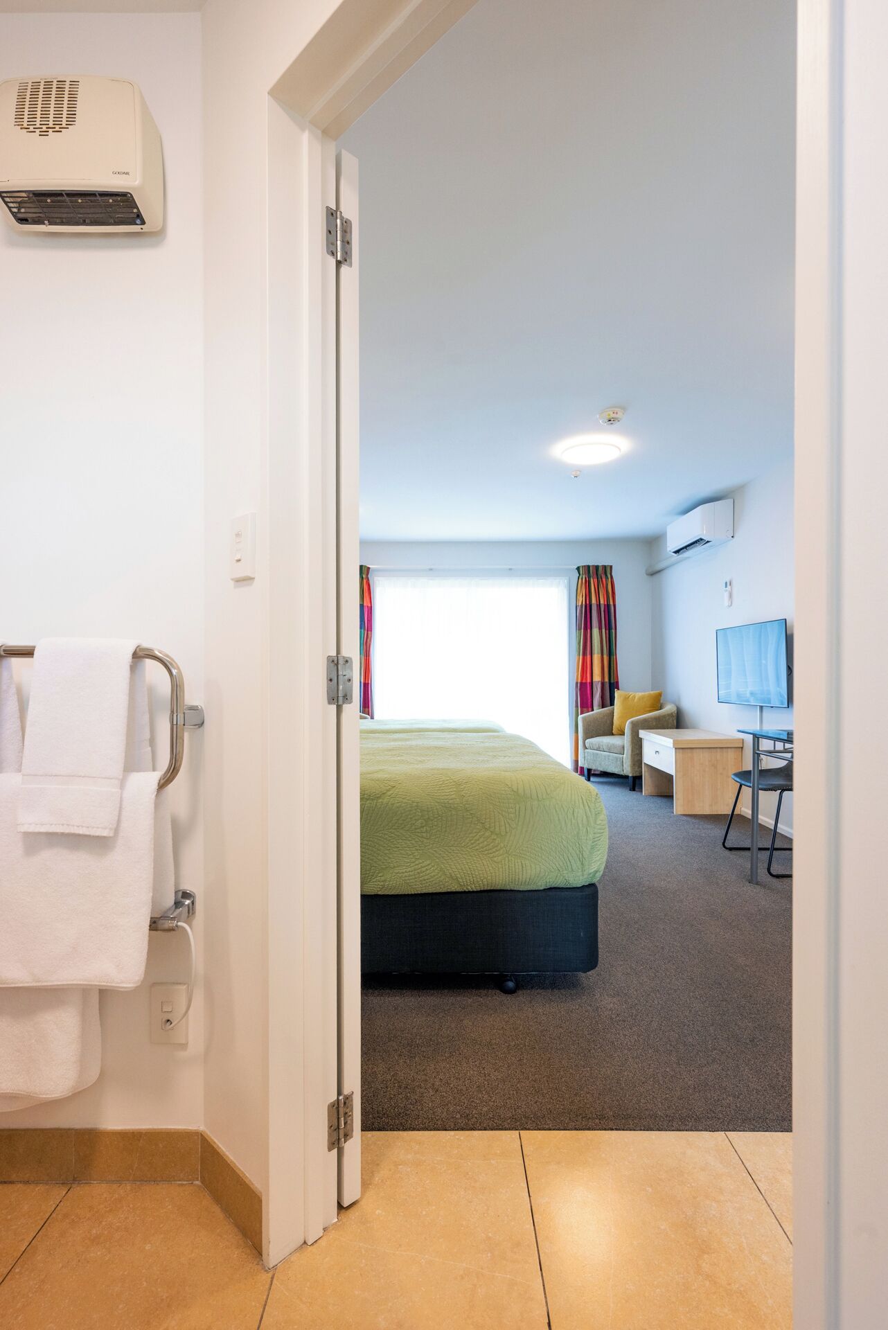 Habitación de hotel con cama, escritorio, silla, televisor y aire acondicionado.