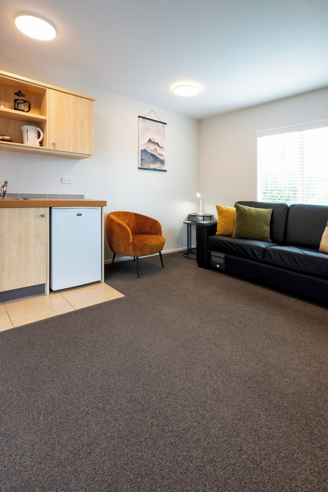 A compact living space with a kitchenette, a sofa, a chair, and a small table.