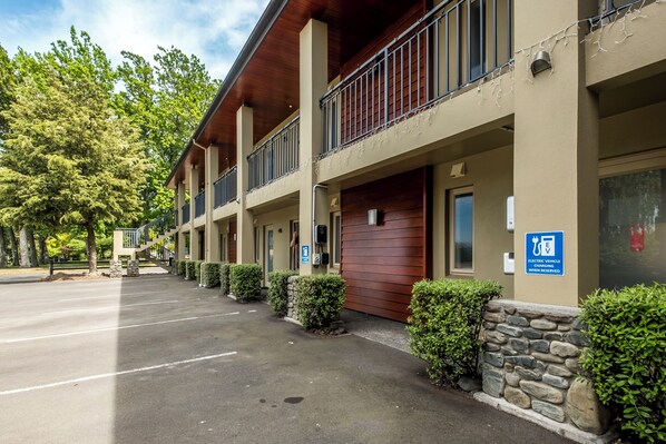 A hotel with a covered outdoor area, stone pillars, and a sign indicating electric vehicle charging is available. - Tussock Peak Lodge (Hanmer Springs)