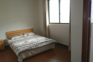 Um quarto com cama de madeira, mesa de cabeceira, janela com cortinas e porta.